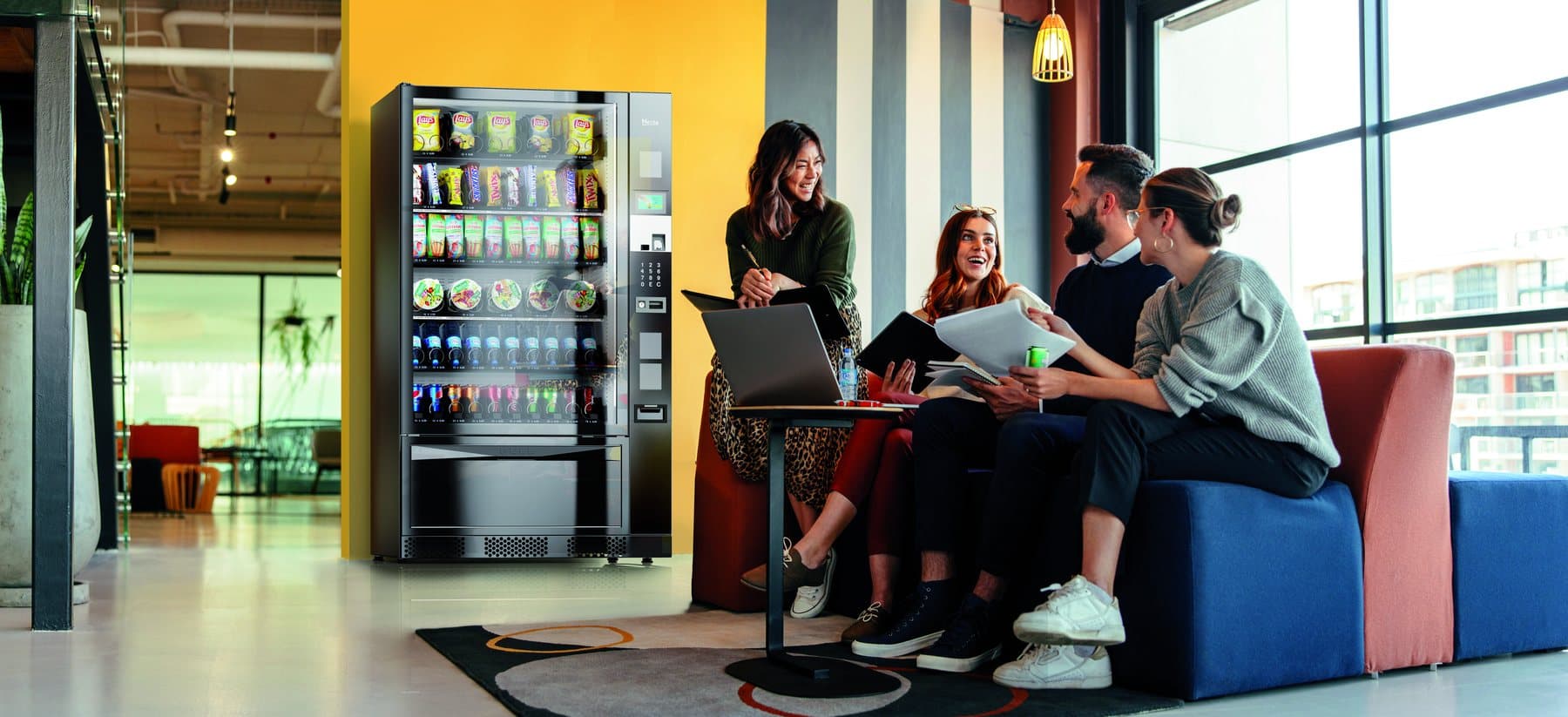 Colleagues sitting beside a Necta Gusto 10 in an office breakout area