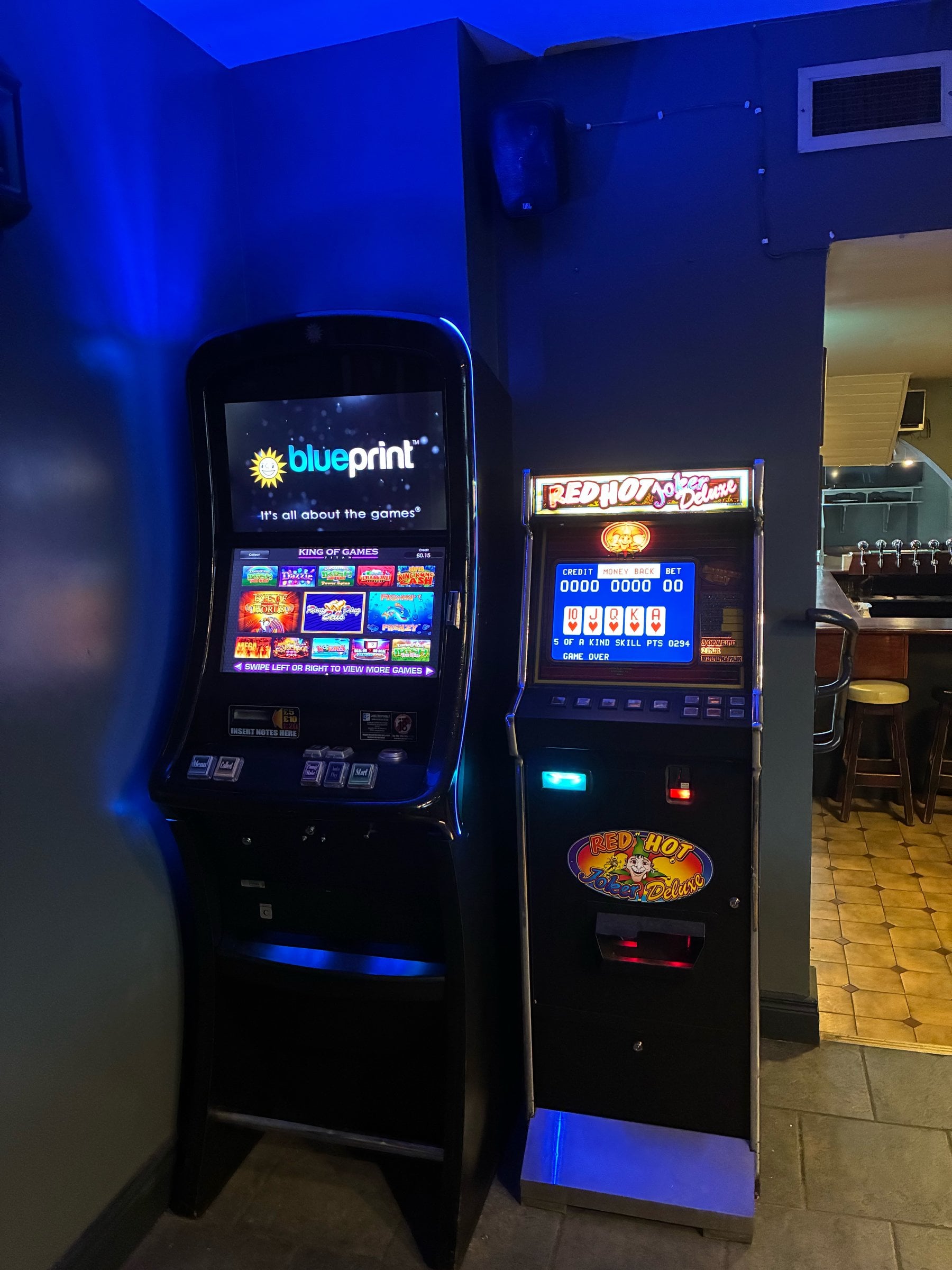 Blueprint pub gaming cabinet beside a Red Hot Joker Deluxe poker machine, on site in a pub with blue lighting